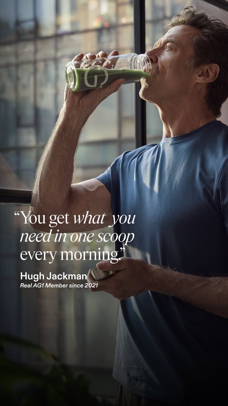 Man in a blue t-shirt drinking a green smoothie from a clear bottle indoors