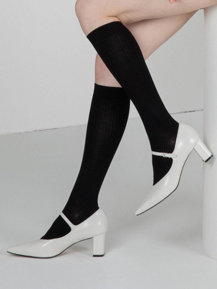Legs wearing black knee-high socks and white Mary Jane heels