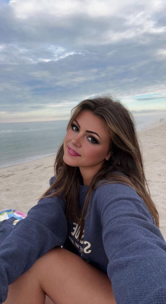 Woman with long hair in a blue sweatshirt smiling on a beach
