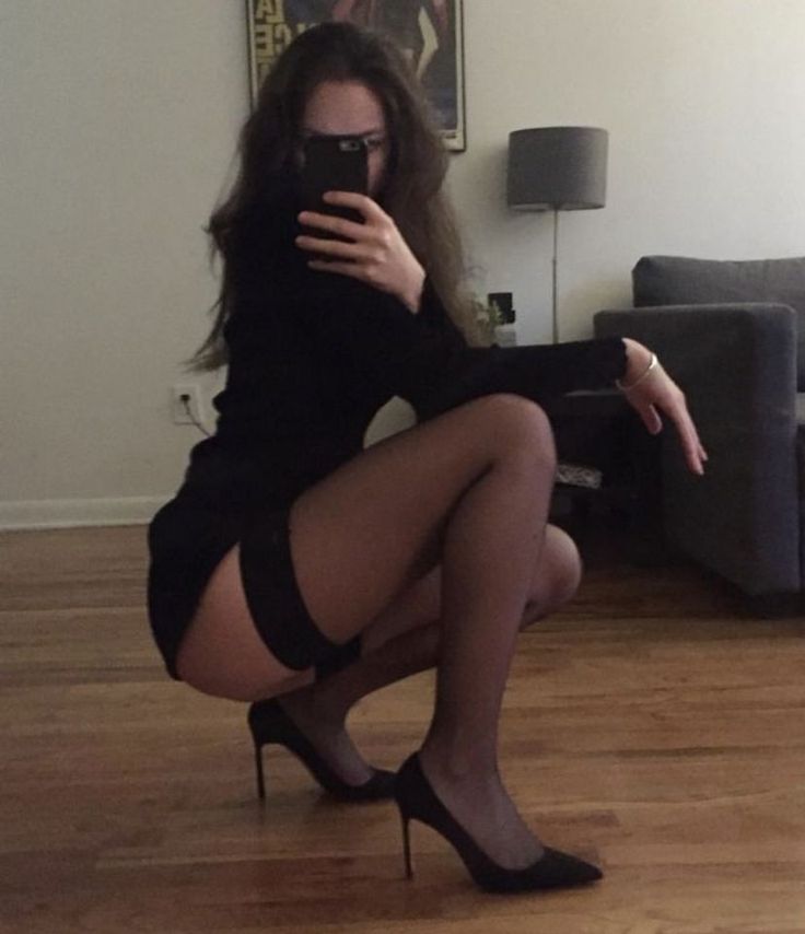 Woman in a black dress and stockings squatting for a mirror selfie