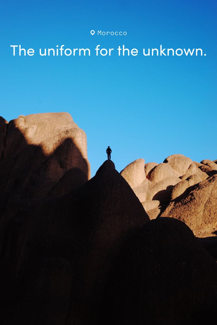 Person silhouetted on a rocky peak in a desert landscape under a clear blue sky