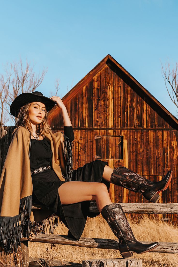 Woman in a cowboy hat and boots sitting on a wooden fence at golden hour