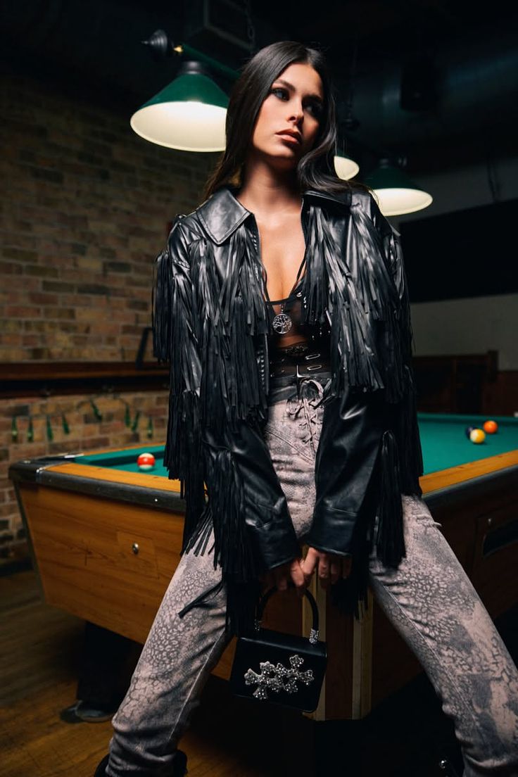 Woman in a fringe jacket and snakeskin pants posing by a billiards table
