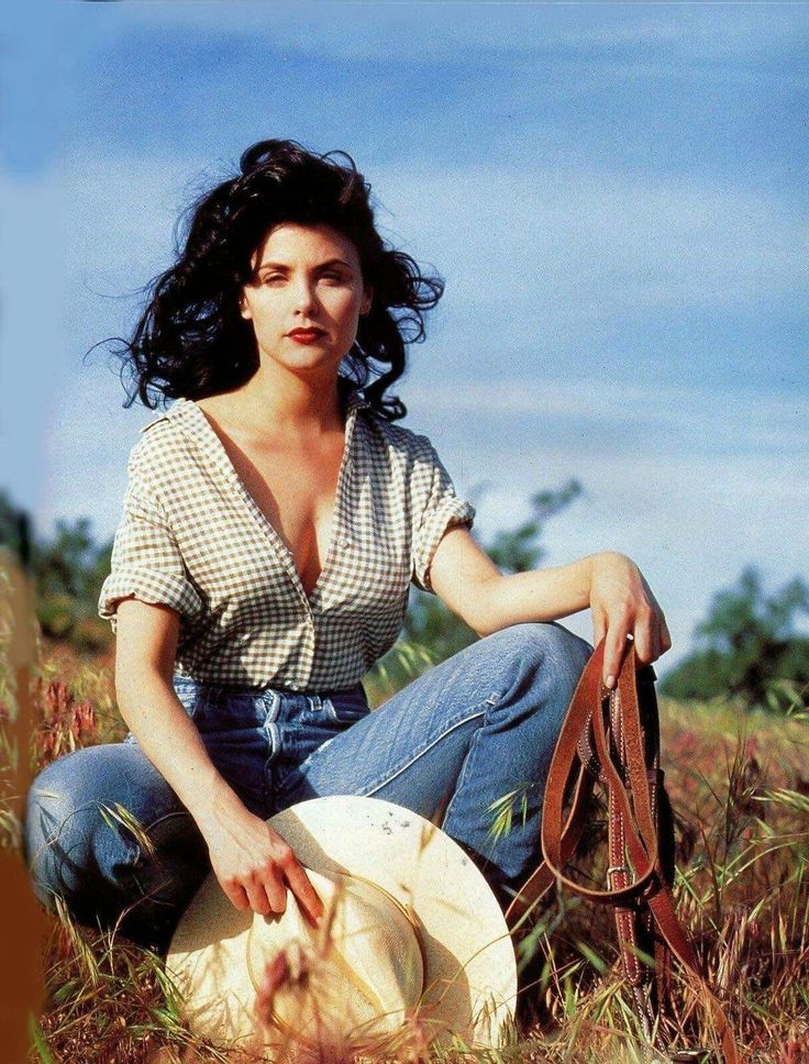 Woman in a gingham shirt and jeans holding a cowboy hat in a field