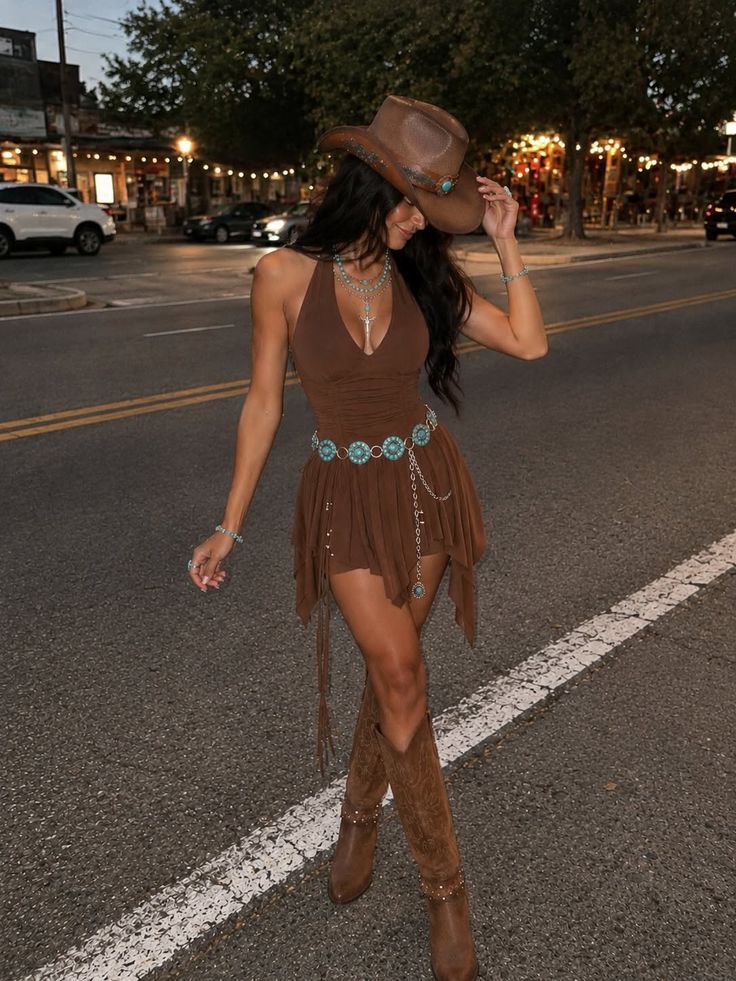 Woman in a brown dress, cowboy hat, and boots on a street at night