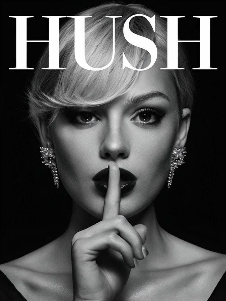 Woman with short blonde hair and dark lipstick, finger to lips, in black and white