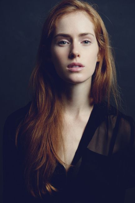 Woman with long red hair wearing a sheer black top, upper body portrait