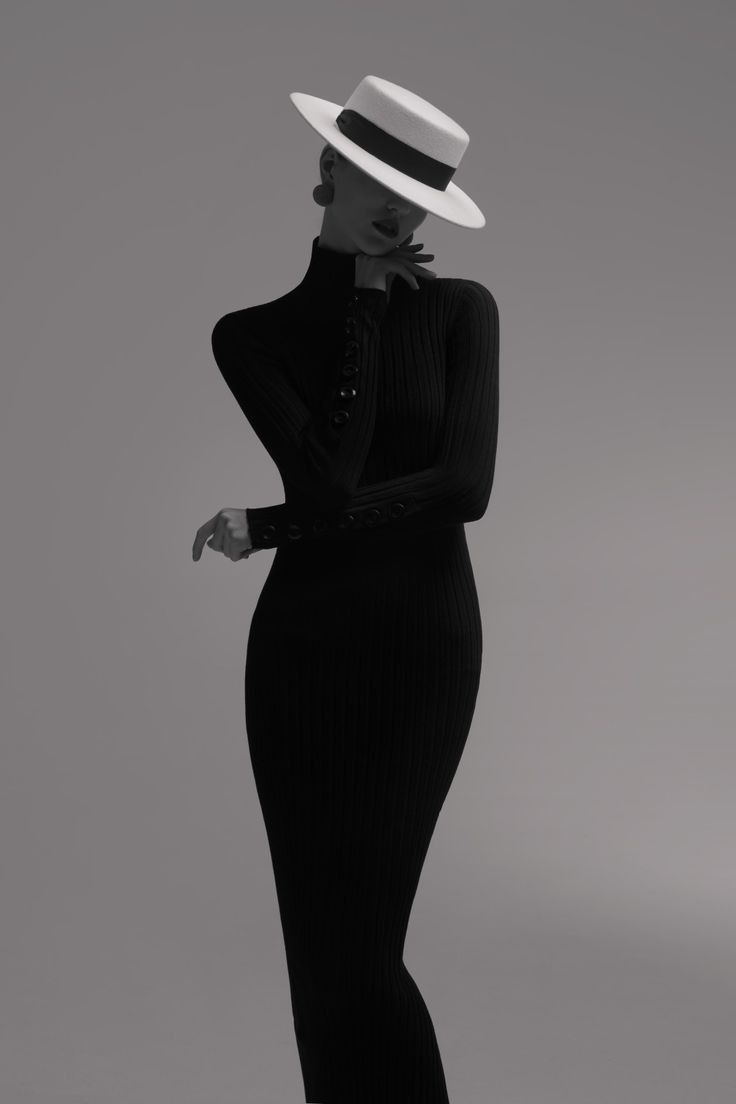 Woman in a black ribbed dress and white hat posing in a studio