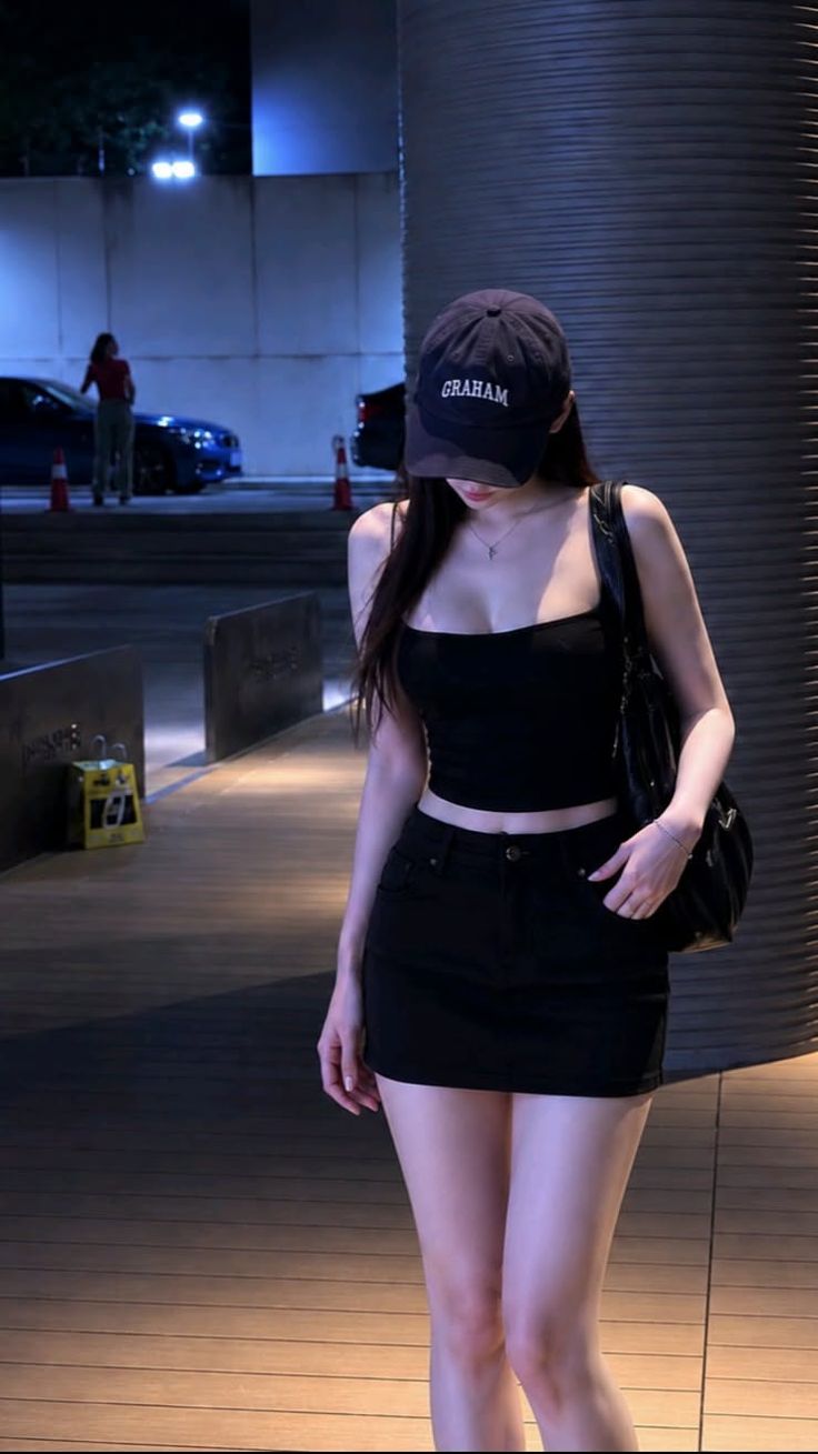 Woman in a black crop top and mini skirt with a baseball cap at night