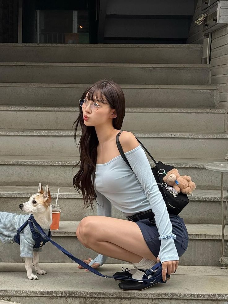 Woman in an off-shoulder top and mini skirt squatting with a dog on stairs