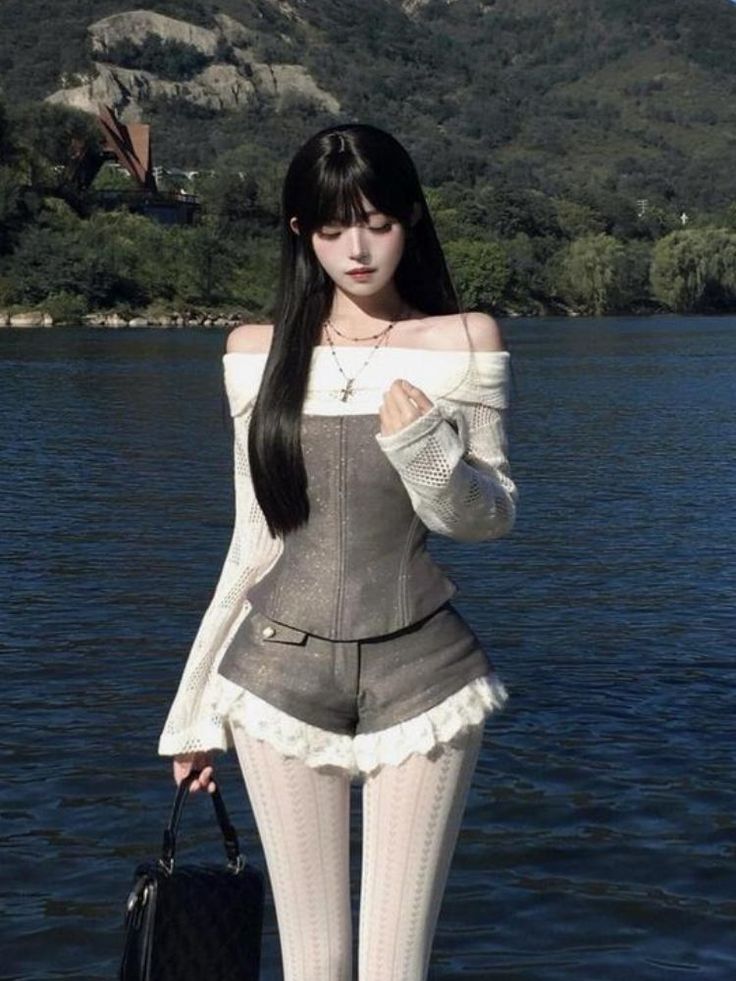 Woman with long black hair wearing an off-shoulder top and shorts by a lake