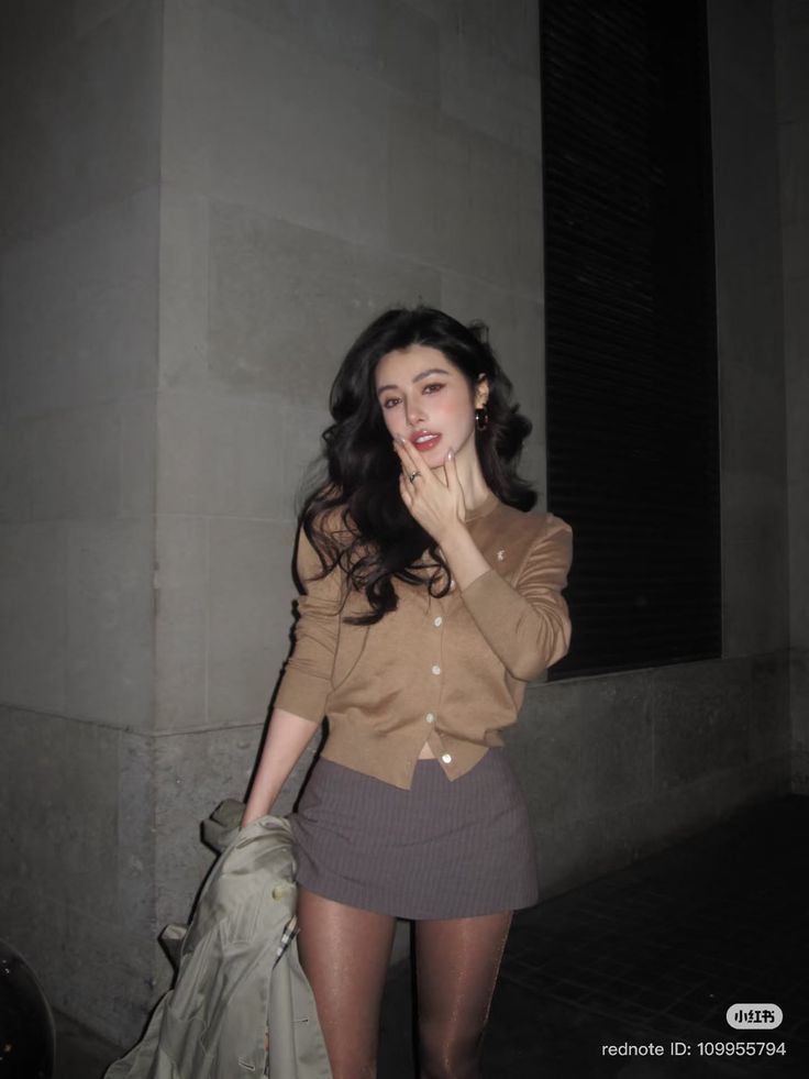 Woman in a cardigan and mini skirt posing outdoors at night