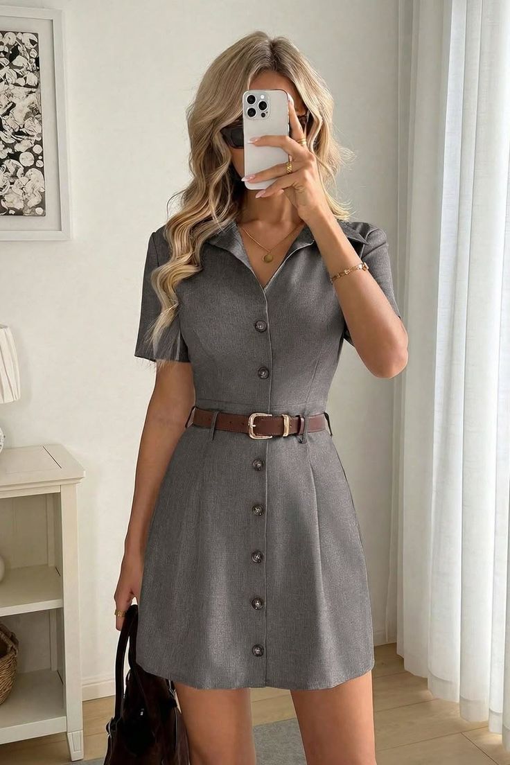 Woman in a gray dress and sunglasses taking a mirror selfie indoors