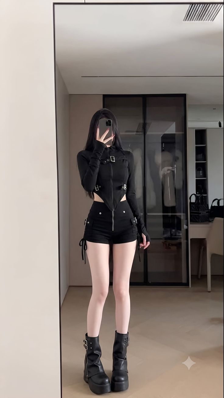 Person with long black hair in a black top and shorts taking a mirror selfie
