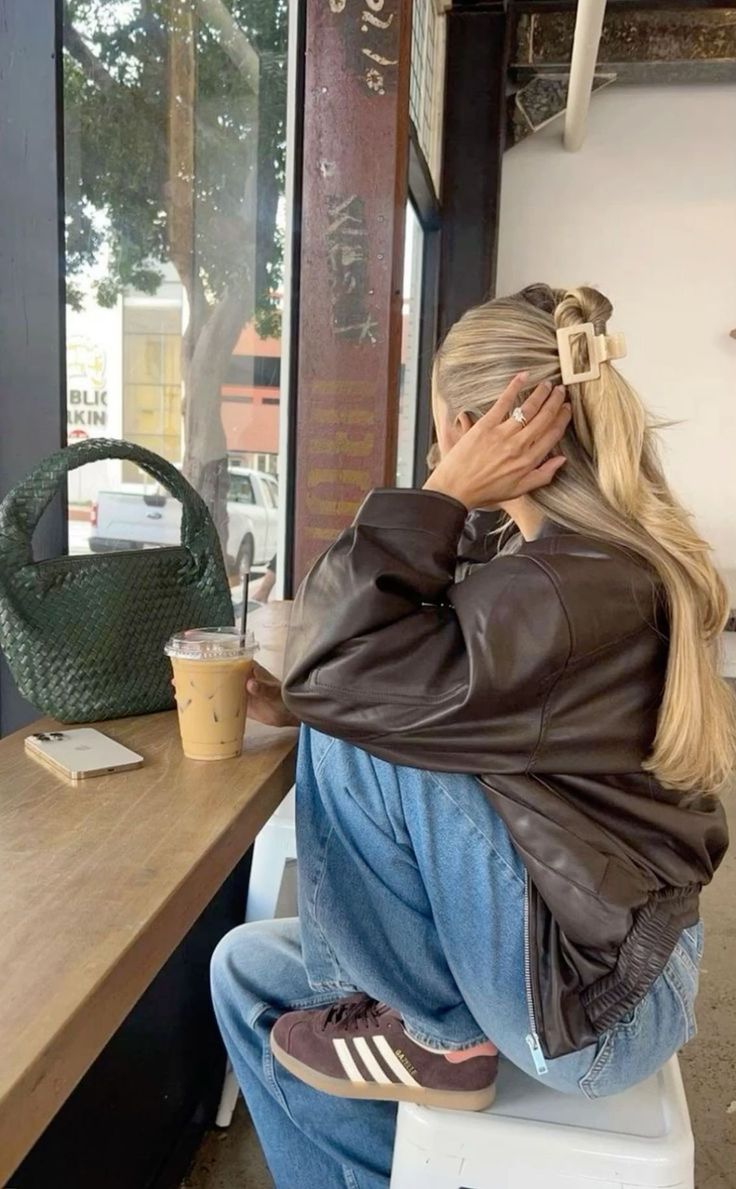 Person in a brown leather jacket and jeans sitting at a coffee shop table