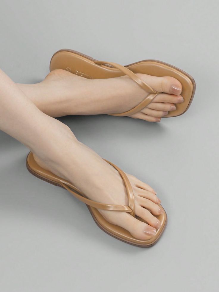Feet wearing tan flip flops with clear nail polish on a gray background