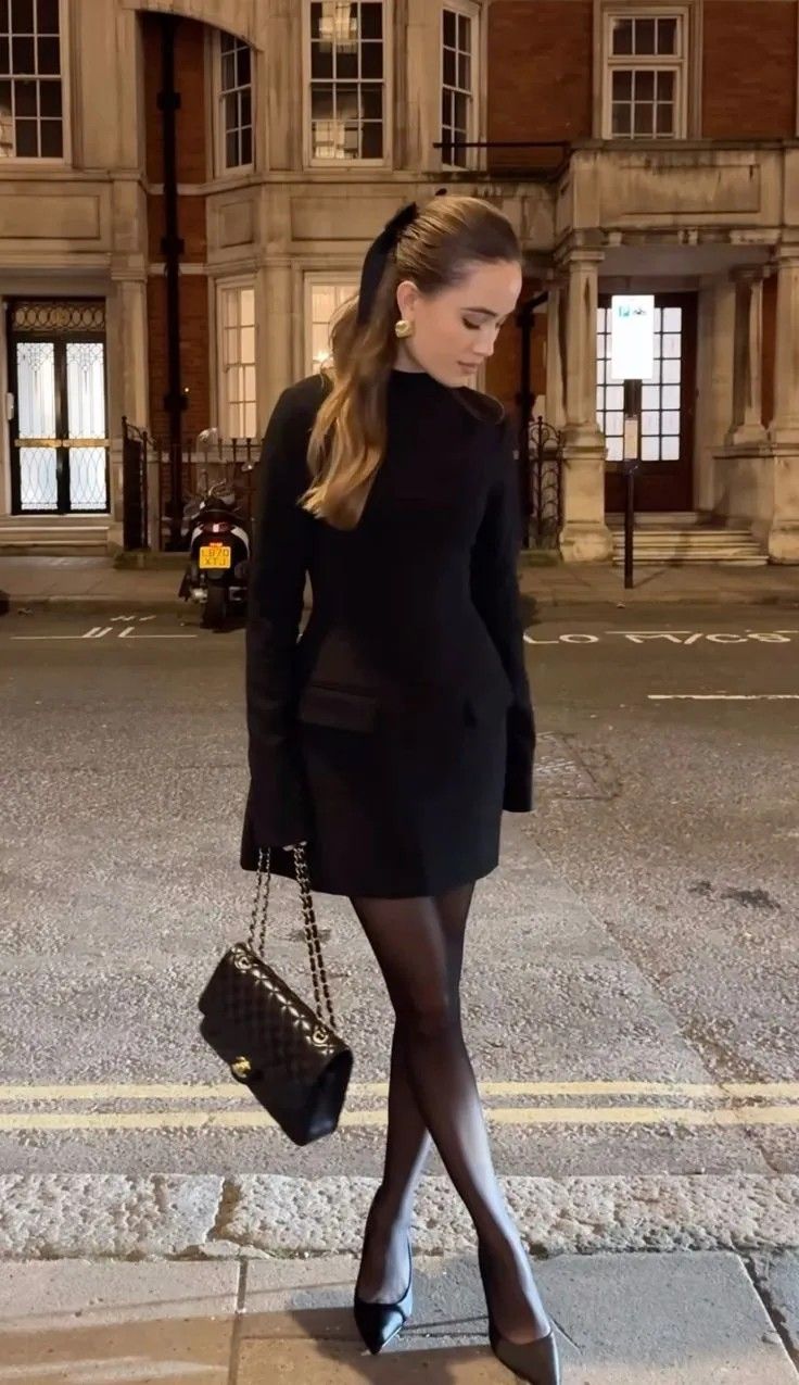 Woman in a black dress and high heels standing on a street at night
