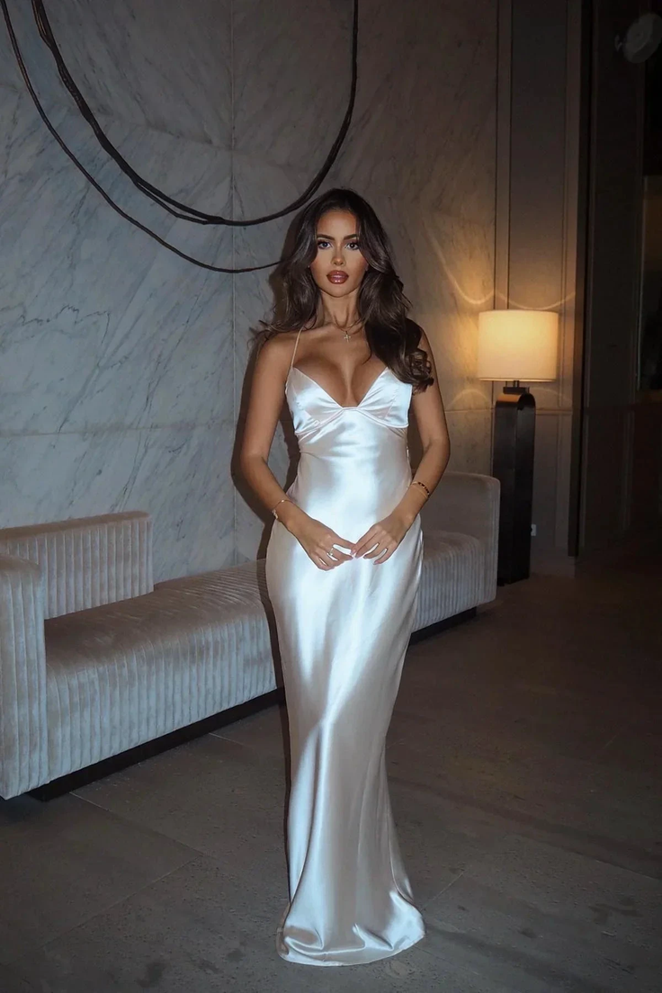 Woman in a white satin dress standing indoors with soft lighting