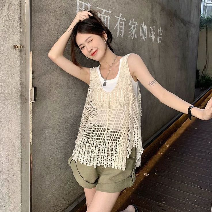 Woman in a crochet top and khaki shorts winking outdoors