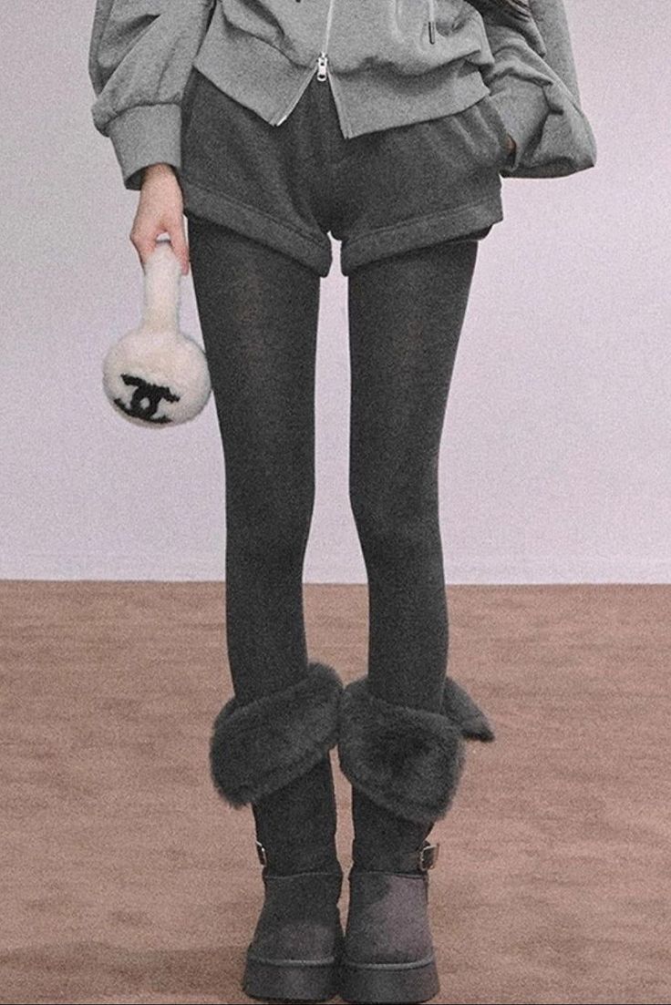 Person in a gray hoodie, shorts, and dark leggings holding a small bag