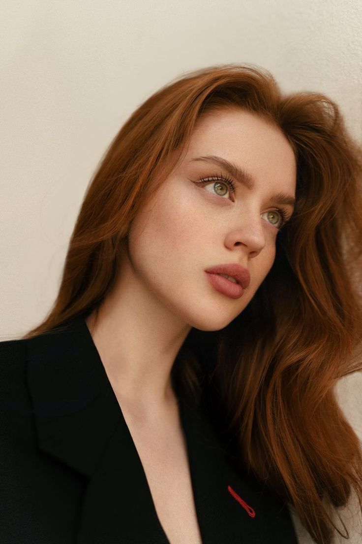 Woman with long red hair and green eyes wearing a black blazer