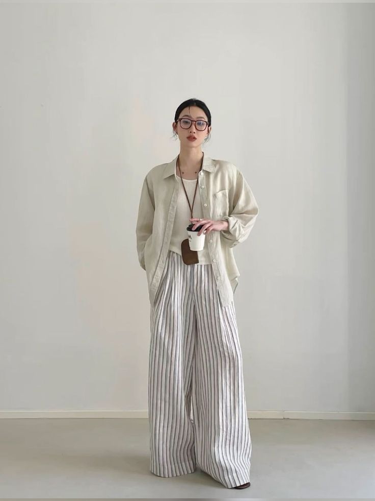 Woman in striped pants and an oversized shirt holding a coffee cup indoors
