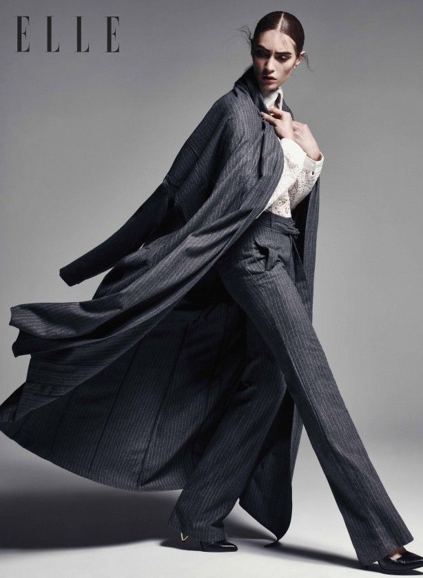 Woman in a pinstripe suit and long coat in a studio setting