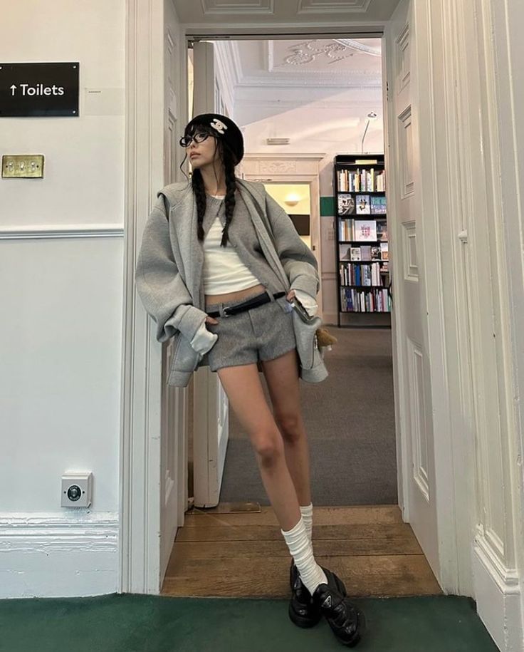 Woman with braids, beret, and glasses wearing shorts and an oversized jacket indoors