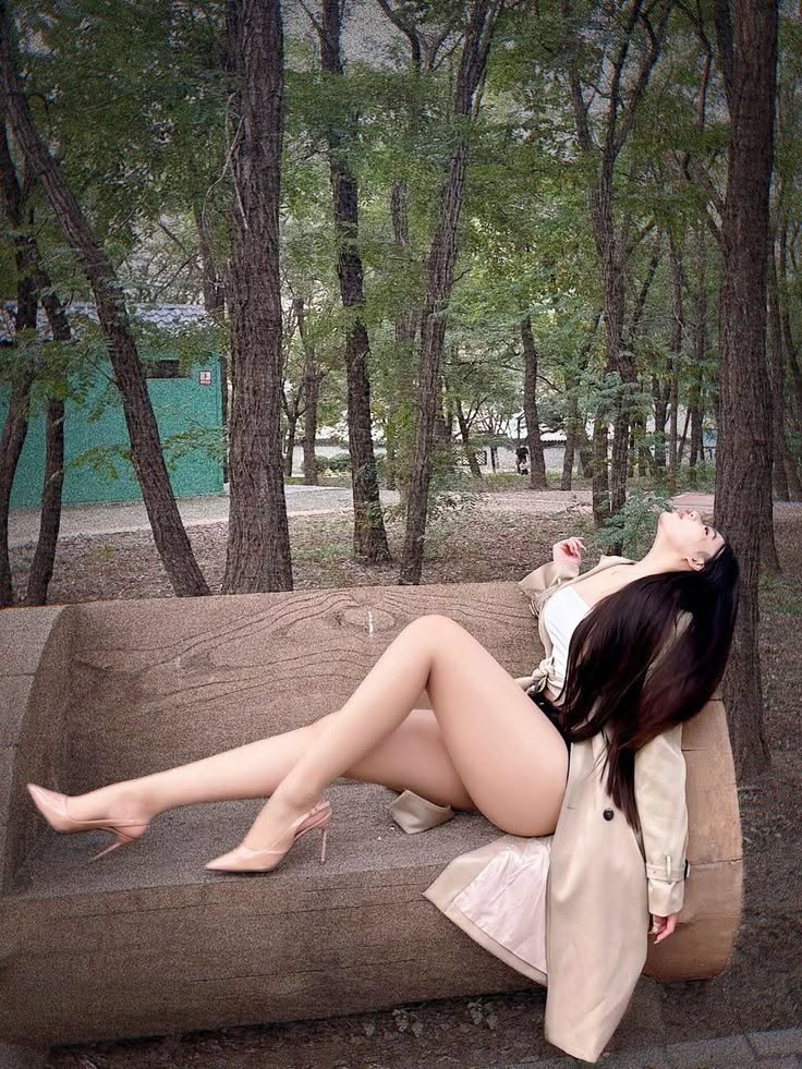 Woman in a trench coat and high heels posing on a wooden bench in a forest