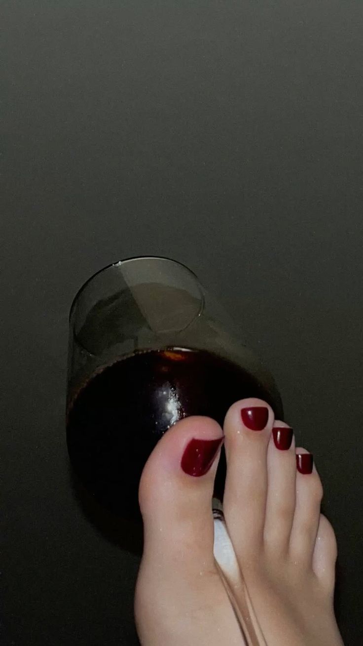 Foot with red nail polish holding a wine glass against a dark background