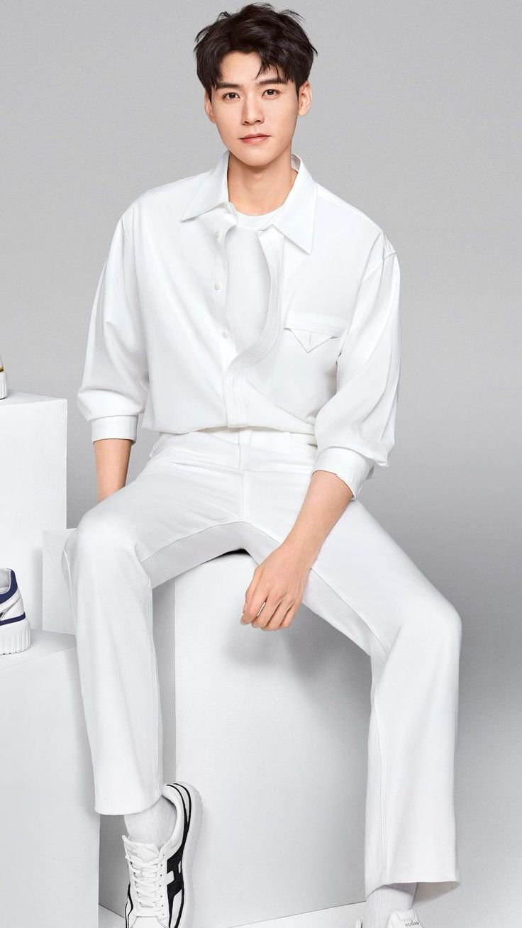 Man in a white shirt and pants sitting on a white cube in a studio