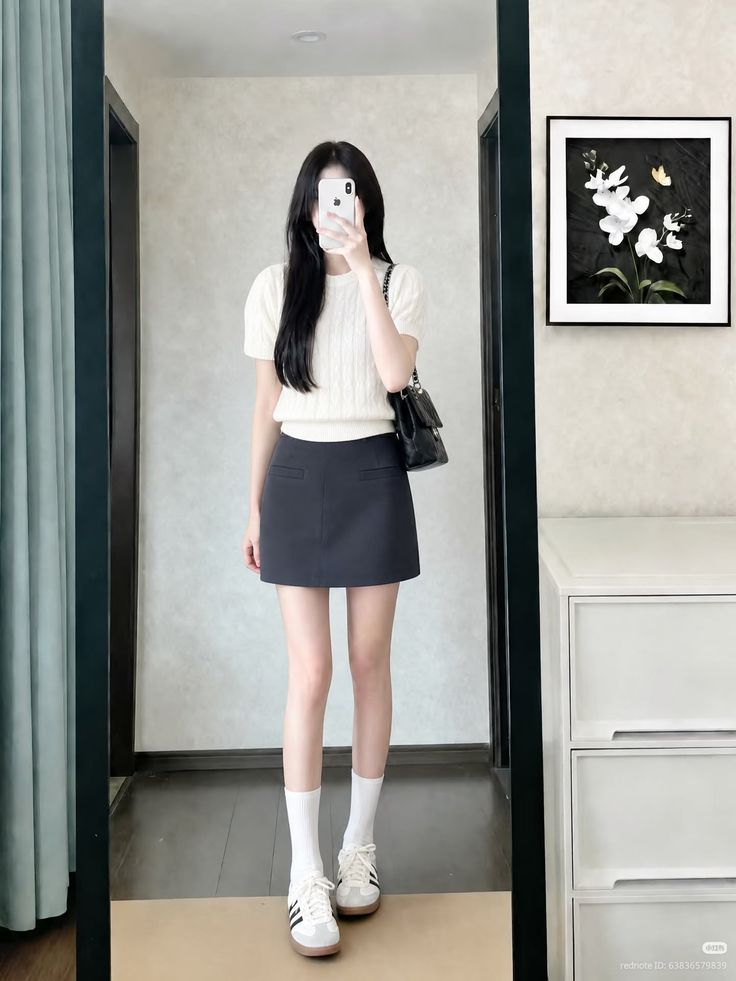 Woman in a white top and black mini skirt taking a mirror selfie