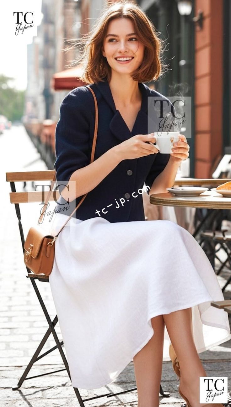 Woman with short hair in a navy jacket and white skirt at an outdoor cafe