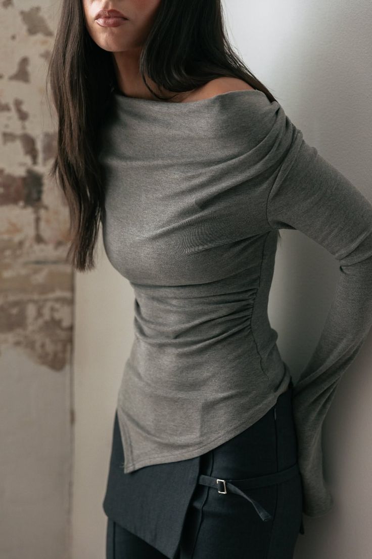Woman with long dark hair wearing an off-shoulder ruched top and dark pants