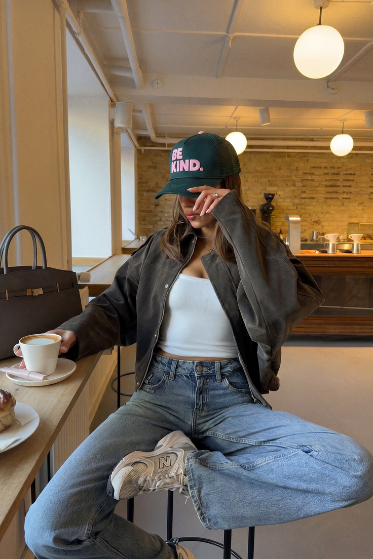 Woman in a baseball cap and jeans sitting at a table in a coffee shop