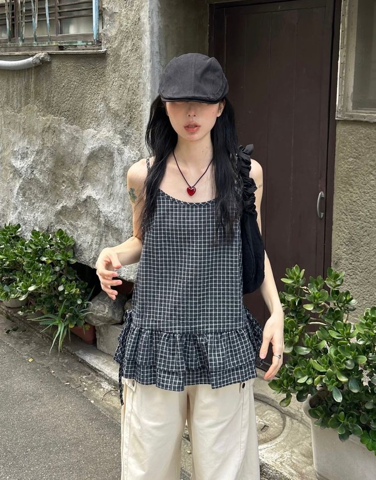 Person in a plaid top and black hat with a heart necklace outdoors