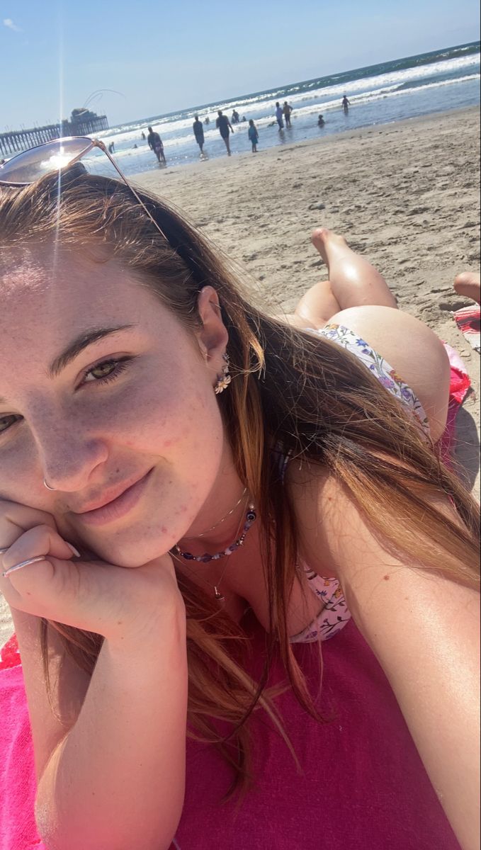 Woman in a bikini lying on a beach towel with a pier in the background