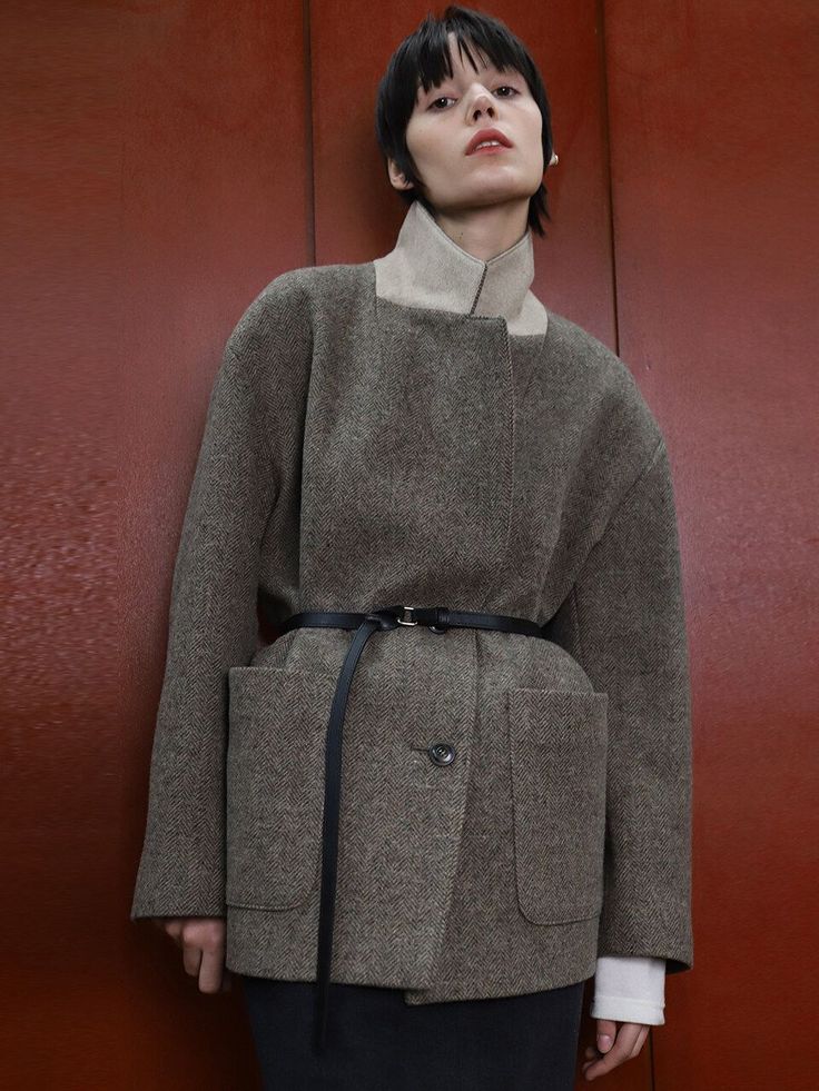 Woman with short hair wearing a belted herringbone coat against a red background