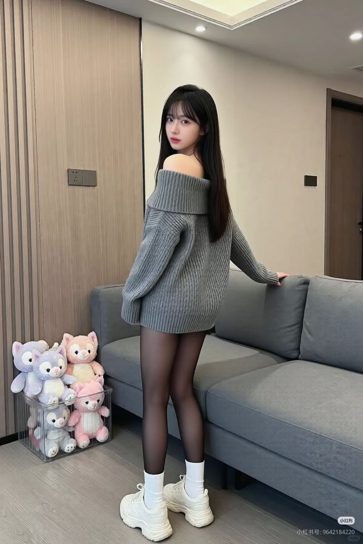 Woman in an off-shoulder sweater and black tights standing indoors