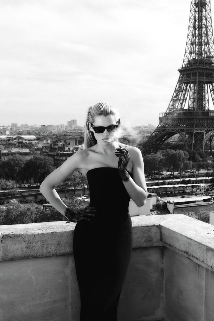Woman in a strapless dress and sunglasses smoking on a rooftop with the Eiffel Tower