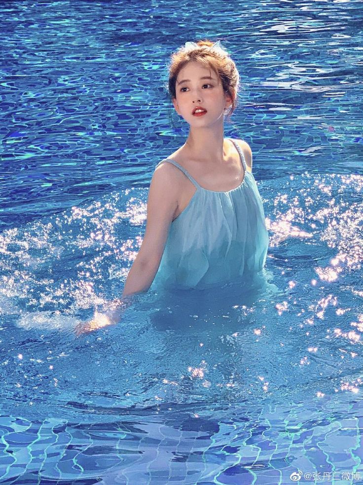 Woman in a light blue dress standing in a sparkling swimming pool