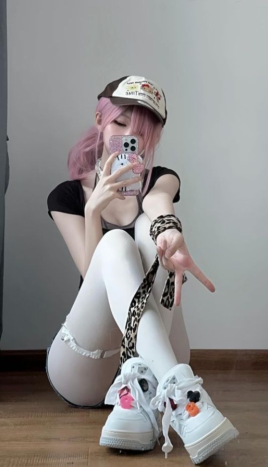 Person with pink hair and a baseball cap taking a selfie while sitting on the floor
