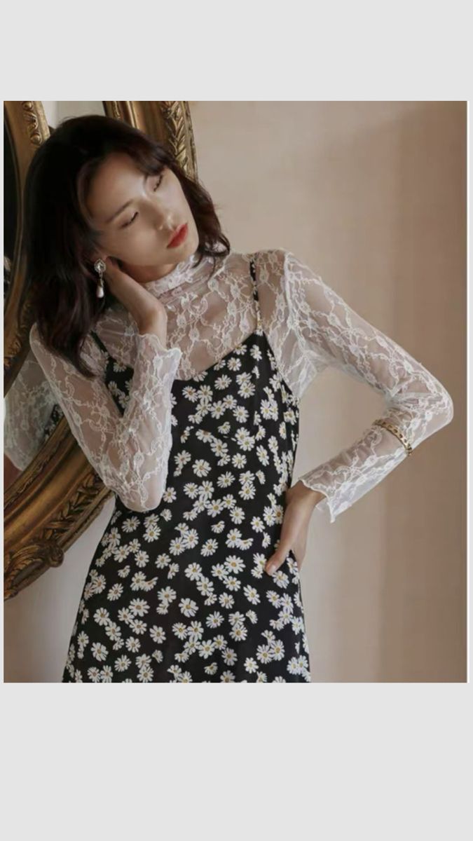 Woman in a daisy print dress and white lace top posing indoors