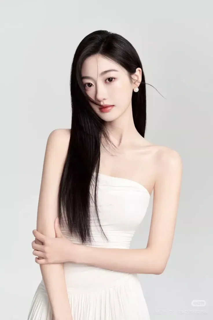 Woman with long black hair wearing a white strapless dress and pearl earrings