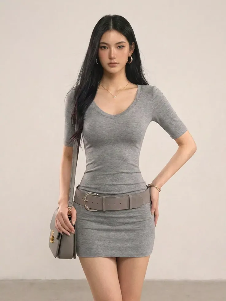 Woman in a gray dress with a belt and shoulder bag posing indoors