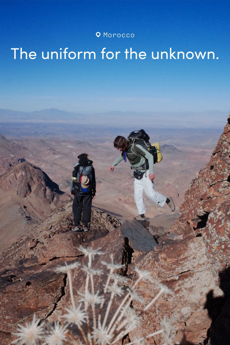 Two people backpacking on a rocky mountain ridge under a clear blue sky