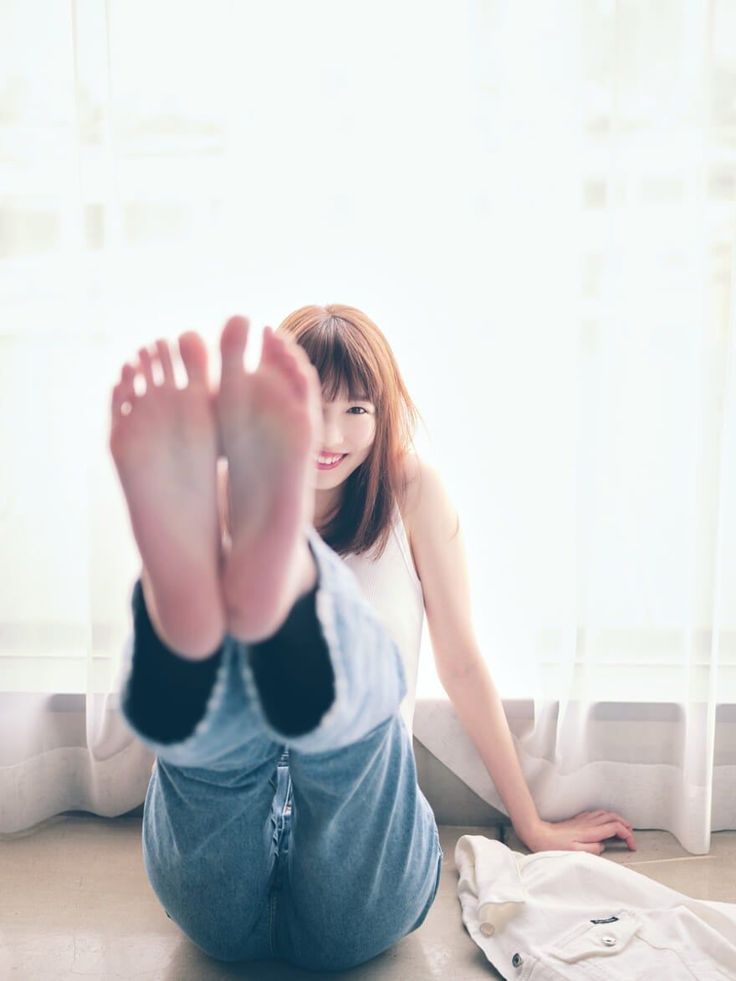 Woman in jeans and a white tank top sitting on the floor with bare feet up