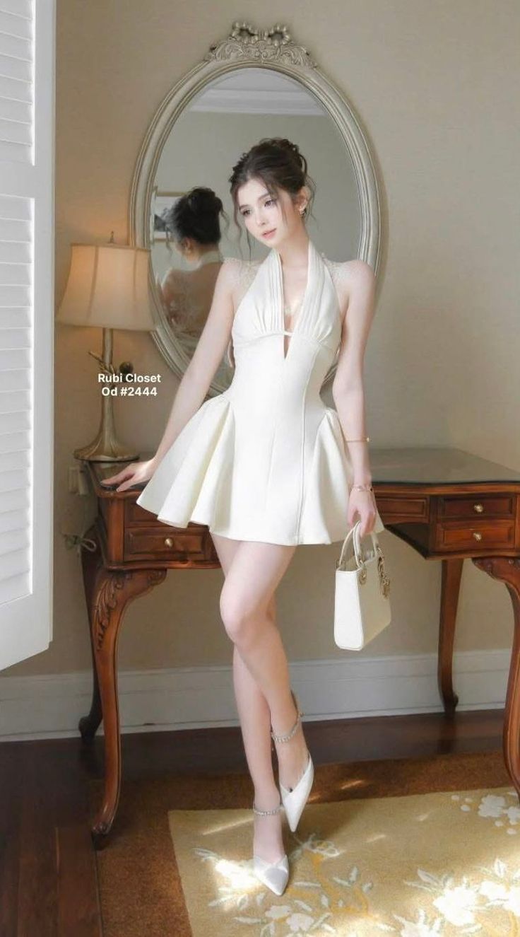 Woman in a white halter neck mini dress and high heels holding a handbag indoors