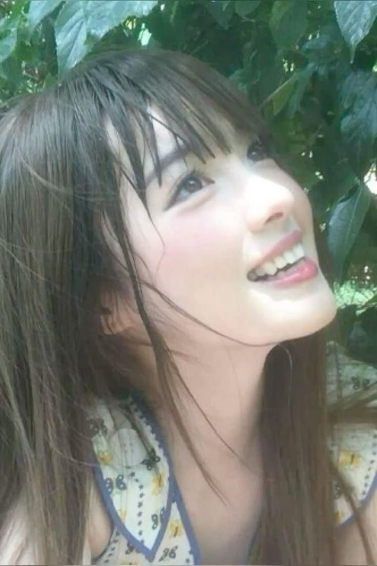 Smiling woman with long hair and bangs looking up, surrounded by green leaves