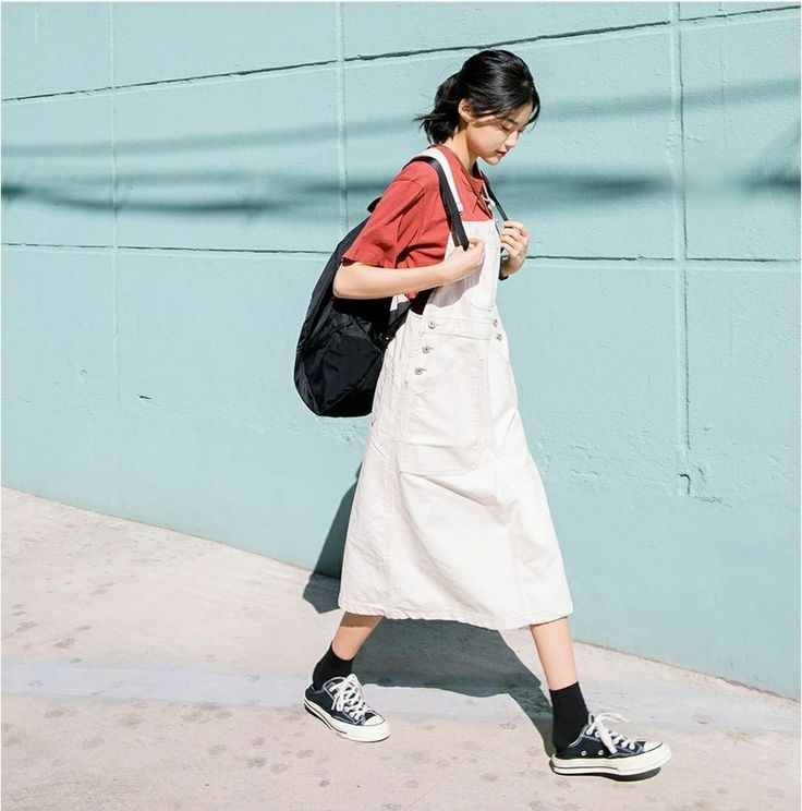 Woman in a white overalls dress and red t-shirt walking outdoors